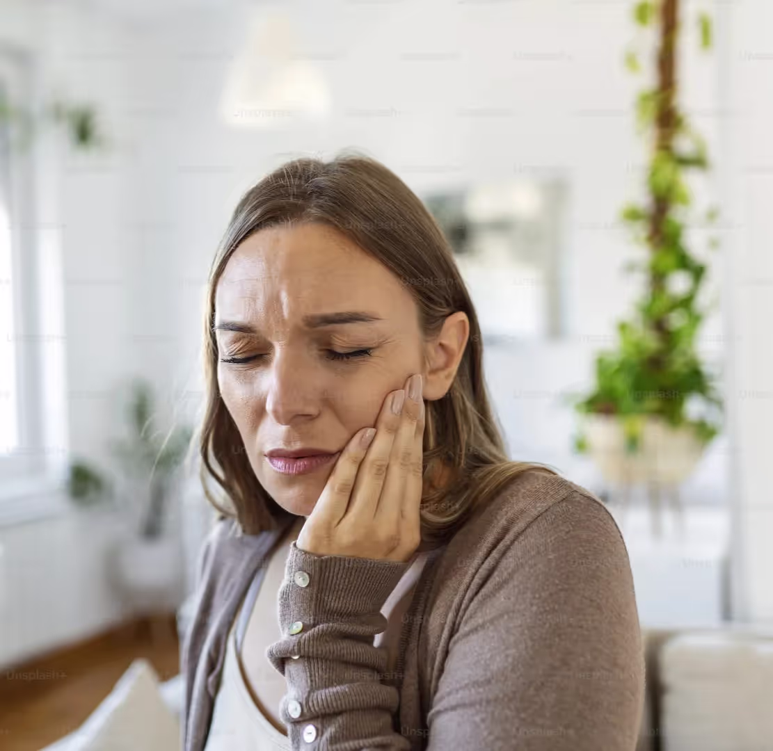 Woman in brown sweater holds her cheek due to tooth pain.
