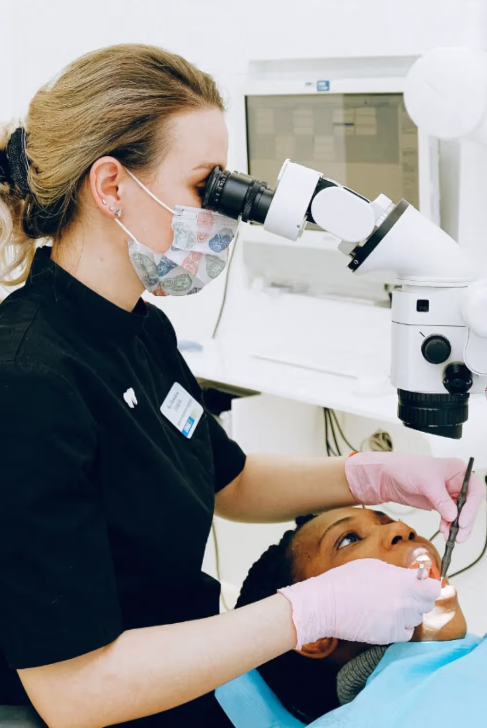 Female dentist looking through a microscope while completing a root canal on a patient.